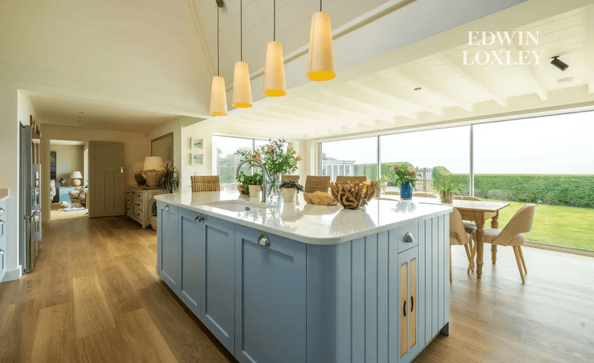 Pale blue kitchen island with pendant lighting and garden view through bifold doors, Seaside Serenity in Middleton-on-Sea