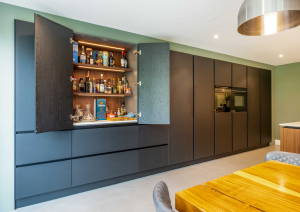 Modern open-plan kitchen dark wall units with ovens and concealed bar area with doors open