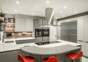 Modern neutral kitchen with handleless furniture with ovens and american fridge freezer. Grey curved breakfast bar with bright red stools.