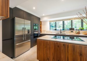 Walnut and matte black modern kitchen with island and yellow stools. Large american fridge freezer